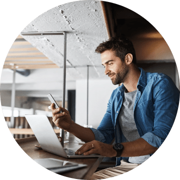 Man looks at smartphone while sitting in front of a laptop computer.